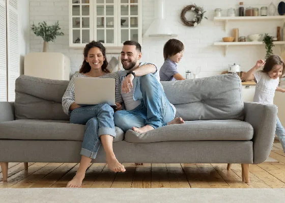 Two parents siting in sofa while kids are playing around couch