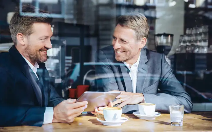 zwei Herren unterhalten sich in einem Café und betrachten einen Tablet-PC